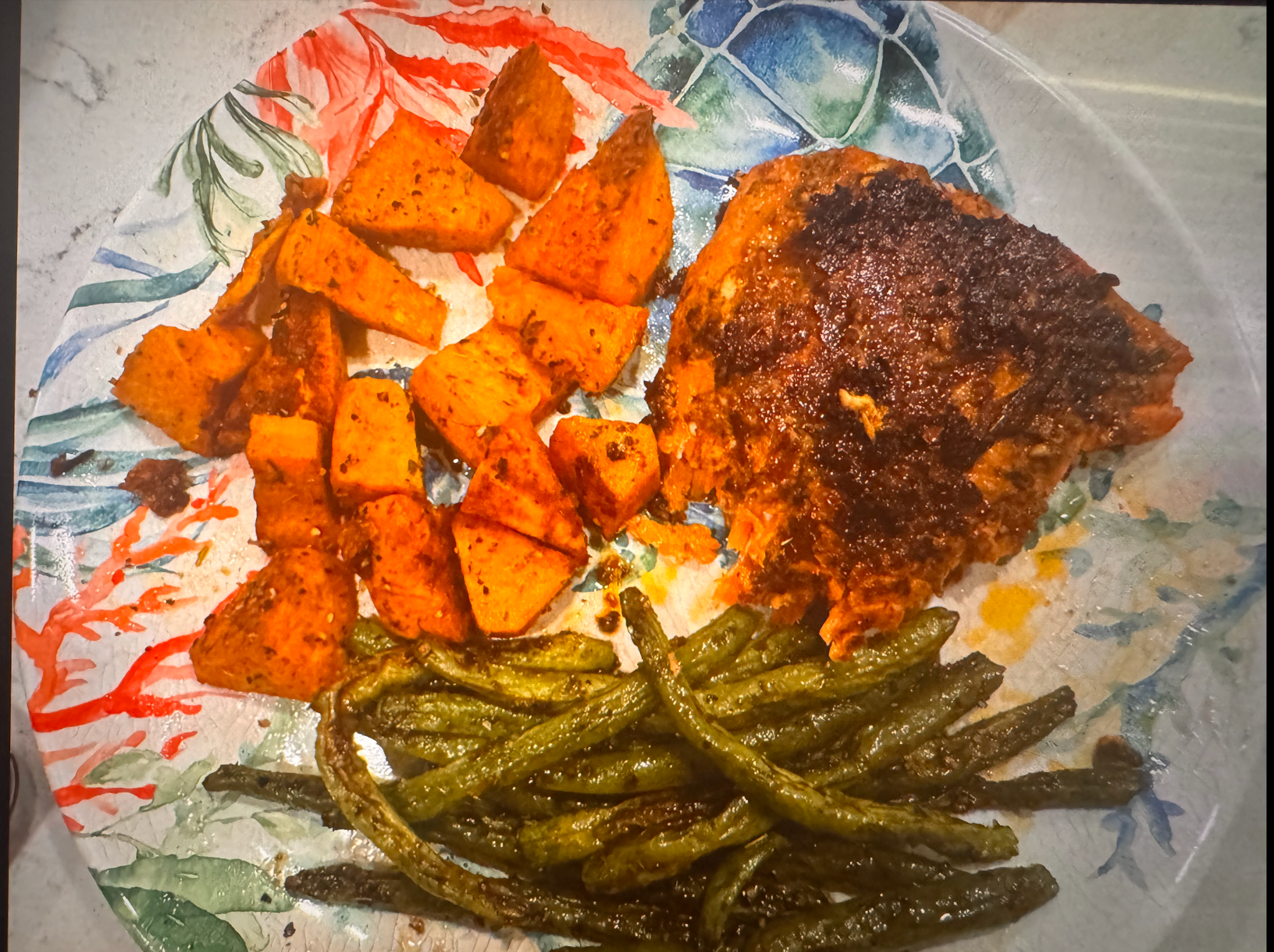 Blackened salmon served with roasted sweet potatoes and green beans on a patterned dinner plate